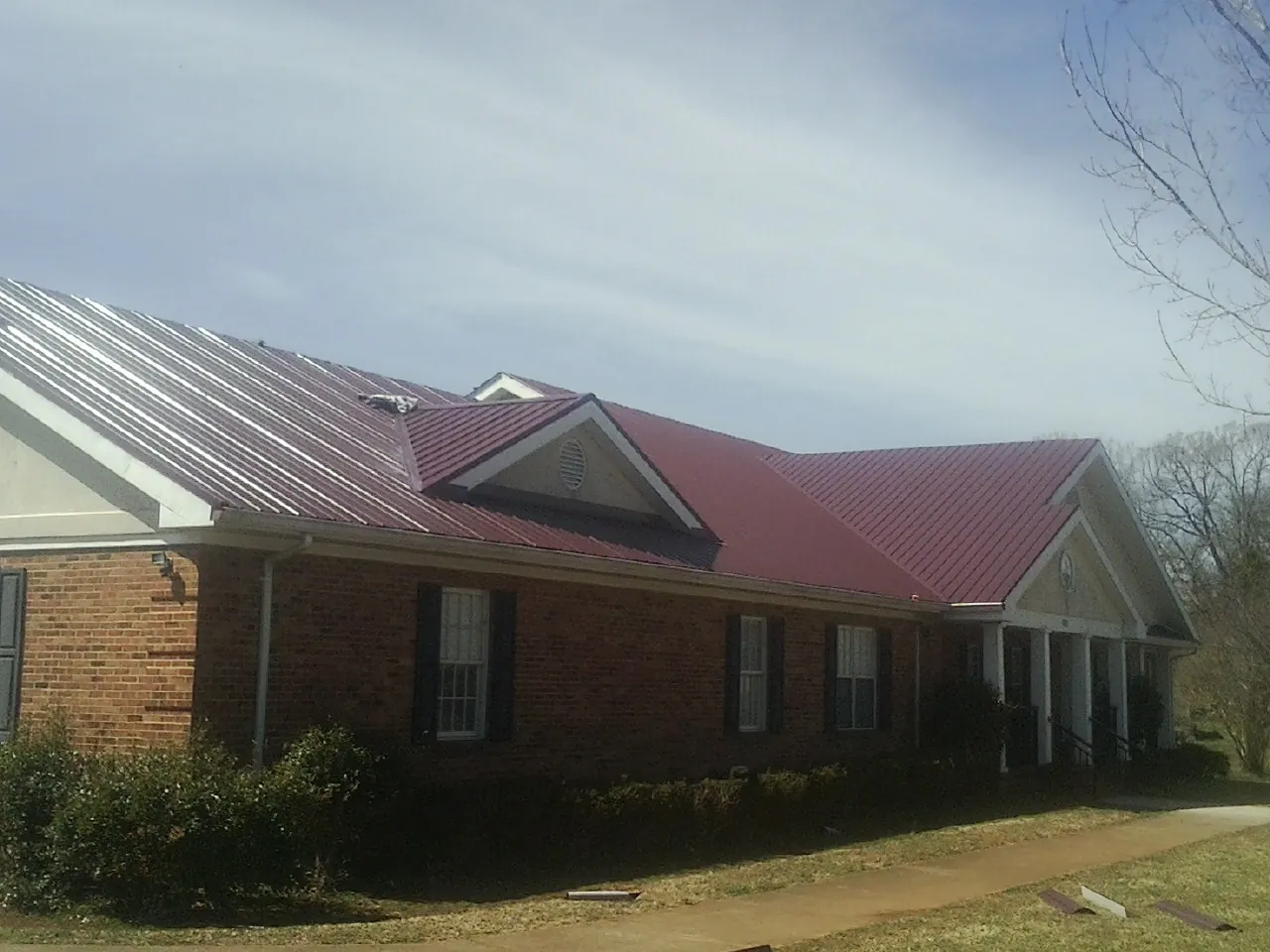 Red metal roof with gabled entries on a long brick building, from a Hail Damage Roof Repair job in Fair Haven