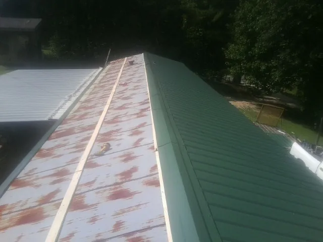 Old rusted panels beside newly installed green metal roofing — Wind Damage Roof Repair by Roofing Brothers in Fair Haven