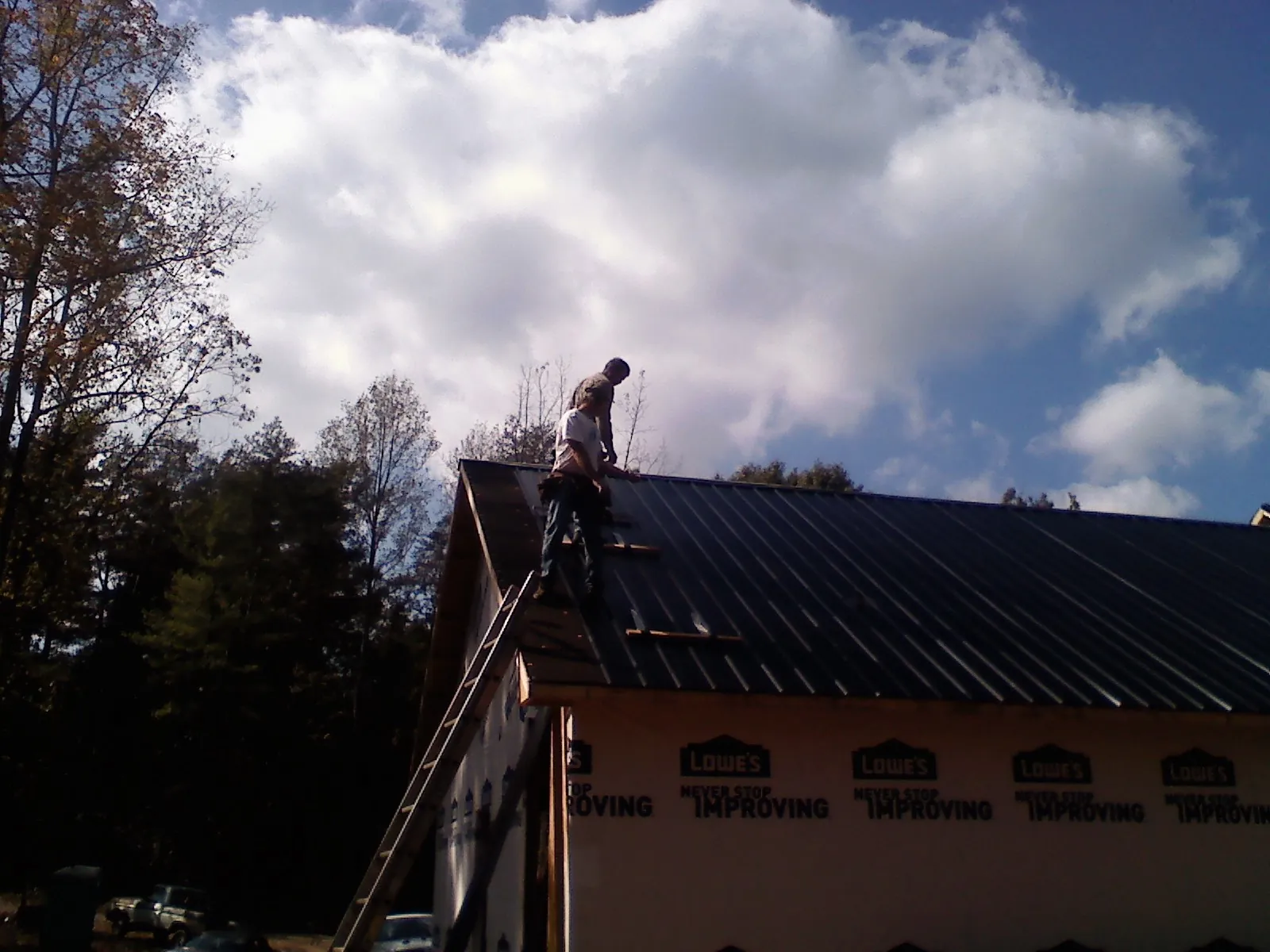 Roofer fastening dark metal panels high against a cloudy sky, from a Roof Inspection job in Fair Haven