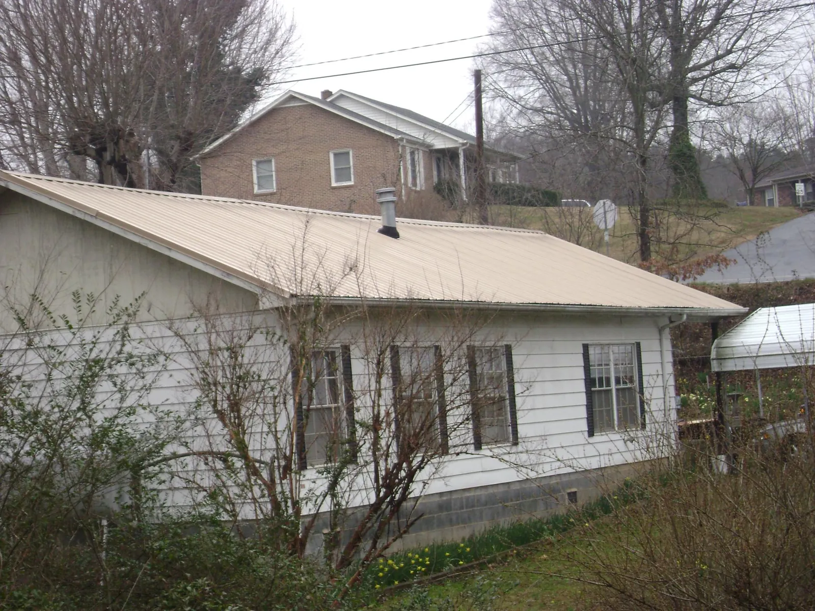 Tan metal roof on a white sided house set into a hillside — Commercial Roofing by Roofing Brothers in Fair Haven