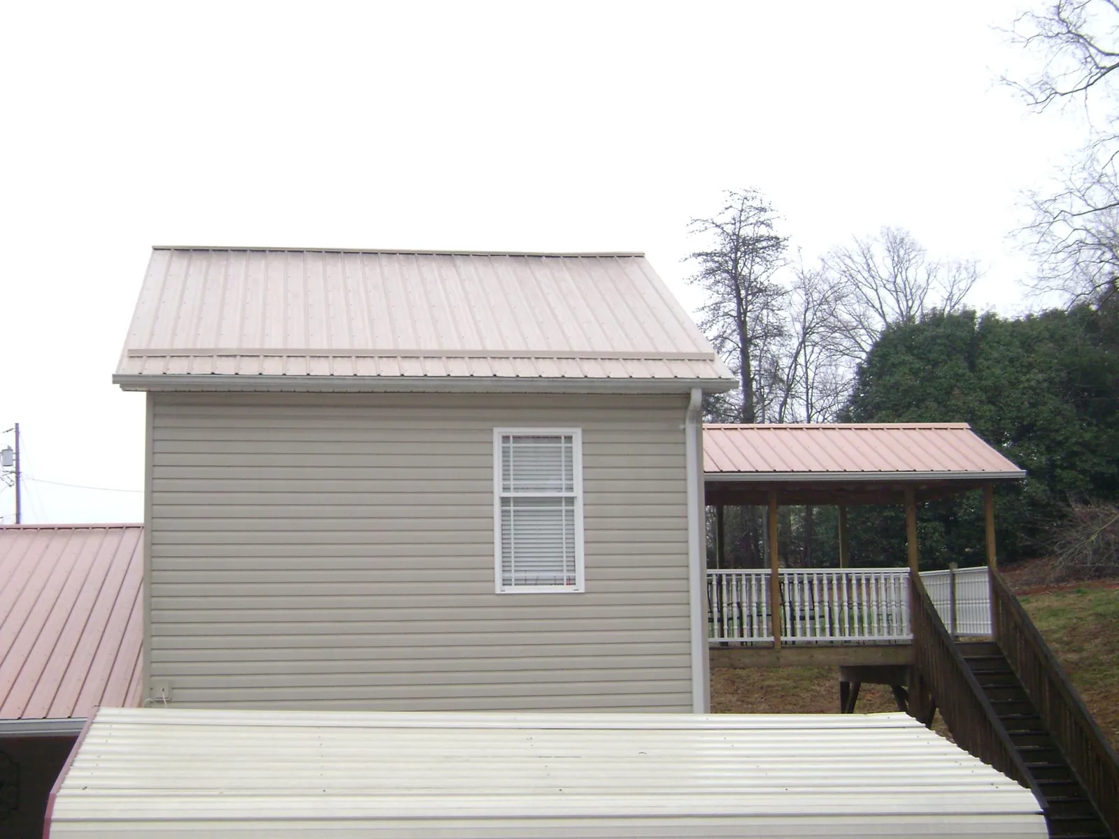 Tan metal roofs on a two story addition and attached porch, from a Roof Replacement job in Fair Haven